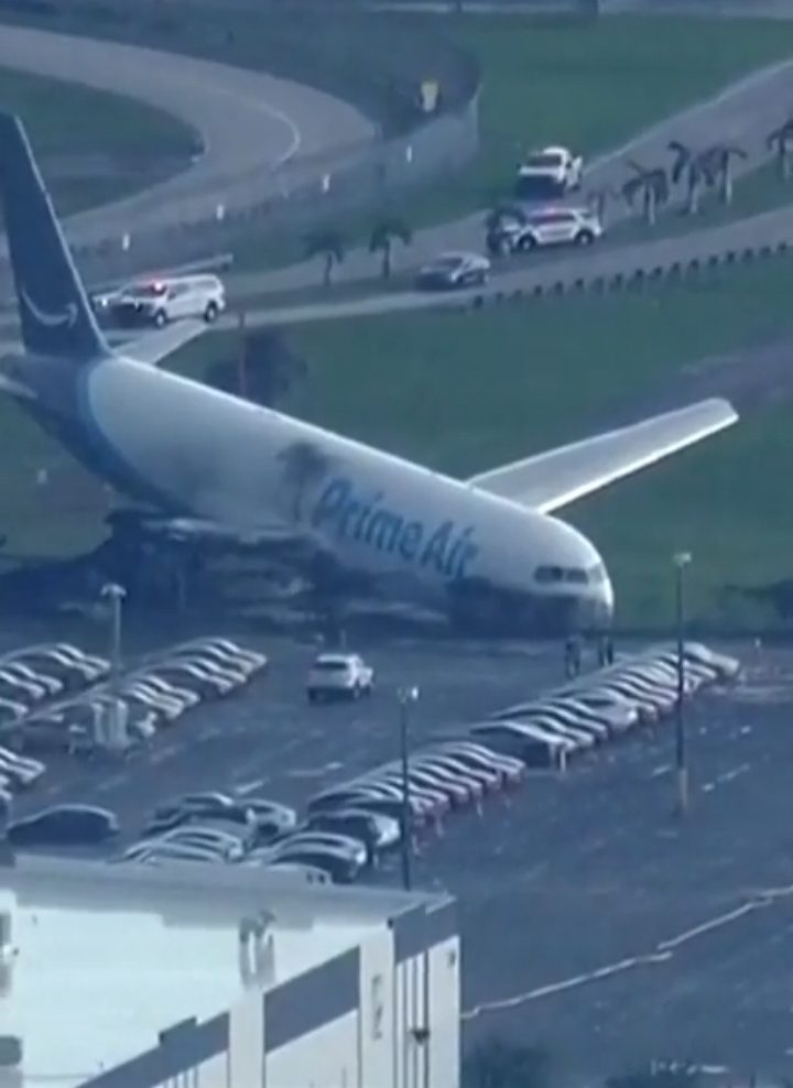 An abandoned Prime Air plane parked in a lot, surrounded by cars and emergency vehicles in the background.