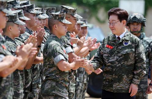 A military leader shakes hands with a soldier during a ceremony, surrounded by other soldiers clapping and showing respect.