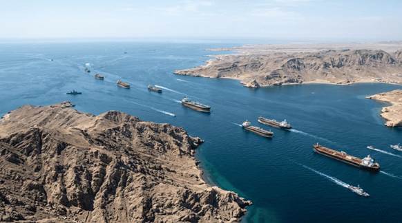 Aerial view of cargo ships navigating through a narrow waterway surrounded by rugged cliffs and desert landscape.