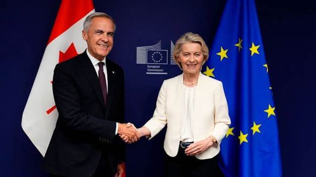 A man and a woman shake hands in front of flags representing Canada and the European Union, suggesting a diplomatic meeting.