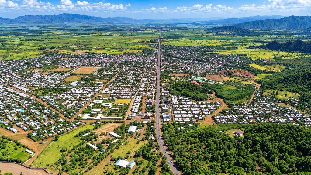 Aerial view of a rural landscape featuring a small town with residential areas, fields, and mountains in the background.