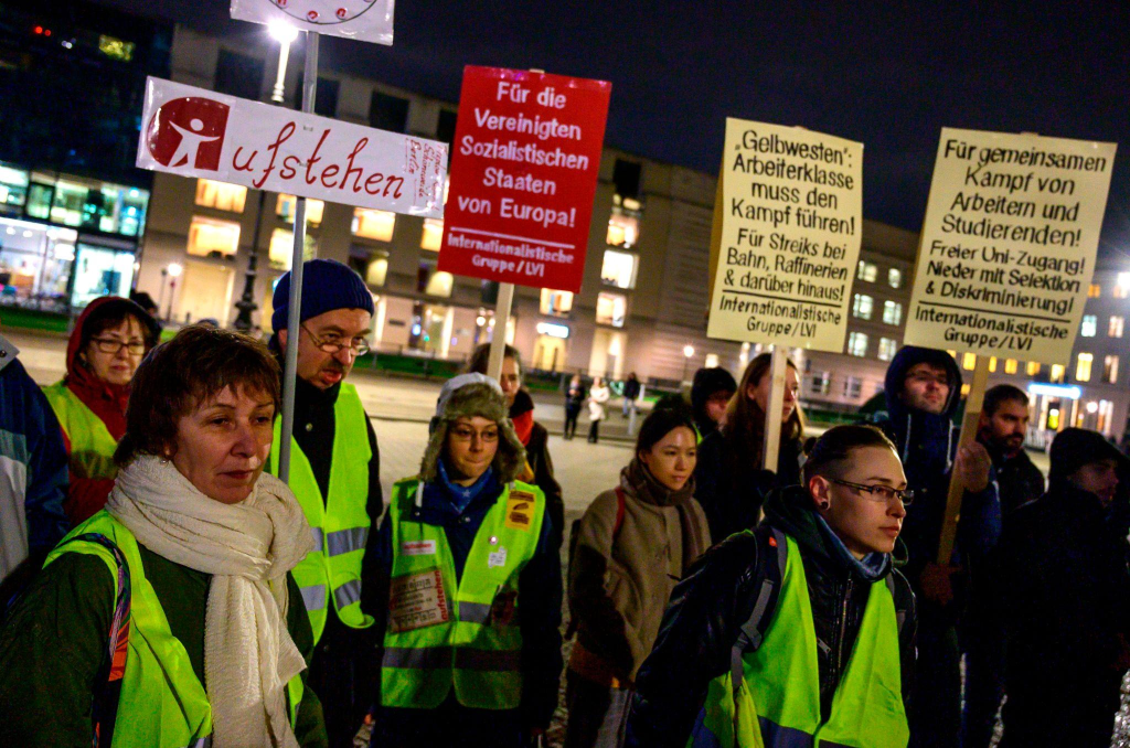 A group of protesters wearing reflective vests gather at night holding signs advocating for workers' rights and social justice in Europe.