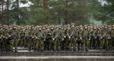 A formation of soldiers in military camouflage uniforms standing in rows, holding rifles, with trees in the background.
