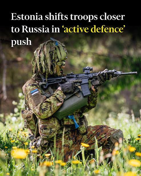 A soldier in camouflage gear crouches in a grassy area, holding a rifle, as part of Estonia's military operations near Russia.